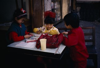 CHINA, Guiyang, Children doing homework outside house.
