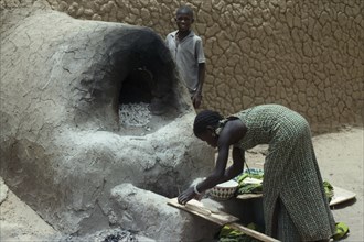MALI, Timbuctu, Girl making bread using outside clay oven.