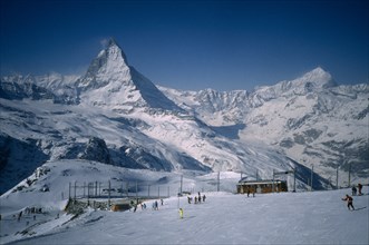 SWITZERLAND, Valais, Zermatt, Skiers on slopes in foreground with Matterhorn behind.