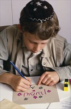 ENGLAND, Religion, Judaism, Boy at Sunday school wearing a kippah and making a card with Hebrew