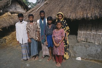 BANGLADESH, Char Kukri Mukri , Family standing outside thatched hut.