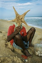 INDIA, Tamil Nadu, Auroville Beach, An elderly sea-shell seller returns to work 5 weeks after the
