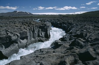 ICELAND, Husafell, River crossing lava field with Langjokull ice cap in the distance
