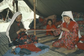 AFGHANISTAN, People, Kirghiz women winding wool inside yurt watched by young girl.