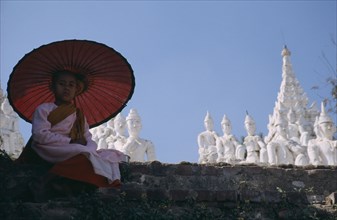 MYANMAR, Mandaly, Buddhist Nun sat on a wall with umbrella at Mingun ancient city.
