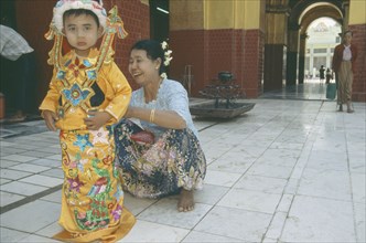 MYANMAR, Mandalay, Young boy being dressed by woman for ordination ceremony Mahamuni Paya. Great