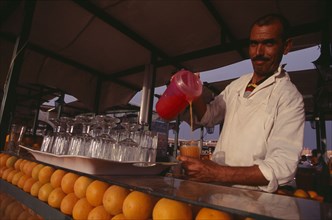 MOROCCO, Marrakech, Dejemma el Fna. A man pouring a glass of orange juice. Rows of oranges and