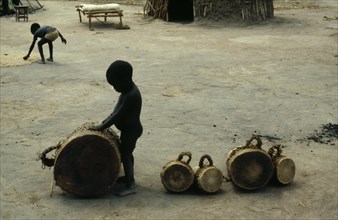 SUDAN, South, Music, Young son of a drum maker playing with finished drums outside hut.