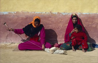 EGYPT, Western Desert, Settled Bedouin woman spinning wool with older woman and child sitting