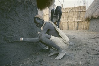 SUDAN, People, Shilluk man plastering exterior wall of mud hut.