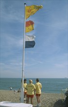 ENGLAND, Hampshire, Portsmouth, Lifeguards on beach under flag pole.