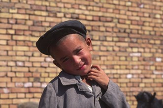 CHINA, Xinjiang Province, Kashgar, Portrait of young Tajik boy standing in front of brick wall