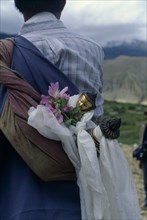 NEPAL, Mustang, Buddha figure wrapped in ceremonial scarves being carried through the summer fields