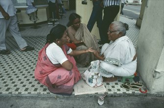 SINGAPORE, Little India, Sidewalk palm reader with women customers on Seragoon Street.