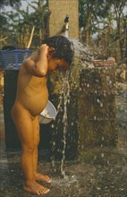 LAOS, Hygiene, Washing, Young Hmong girl washing under stand pipe in Hmong returnee villages for
