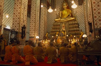 THAILAND, Bangkok, "Monks pray, kneeling down in front of large golden Buddha at Wat Arun. The