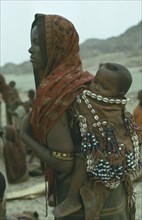 ETHIOPIA, Children, Carrying, Danakil tribeswoman carrying baby on her back in sling decorated with