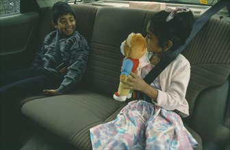 ENGLAND, London, Children, Two Bengali children in back seat of car wearing seat belts.  Young girl
