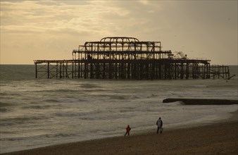 ENGLAND, East Sussex, Brighton, The ruined West Pier with a man and small child walking together