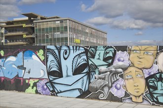 ENGLAND, East Sussex, Brighton, Colourful graffiti on wall with tall buildings behind.
