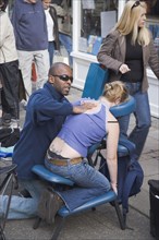 ENGLAND, East Sussex, Brighton, Masseur performing massage in East Street on a woman customer sat