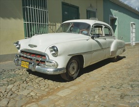 CUBA, Havana, Trinidad de Cuba, A white Chevy sits amidst the town’s features of cobblestone
