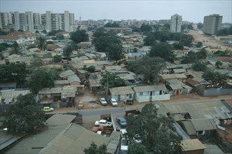 ANGOLA, Luanda, Cars parked next to houses along a road with high rise apartment blocks in the