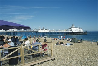 ENGLAND, East Sussex, Eastbourne, Beach cafe with people sat on chairs under parasols infront of