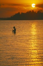 CUBA, Bay of Pigs, Line fisherman standing waist deep in water silhouetted against deep orange