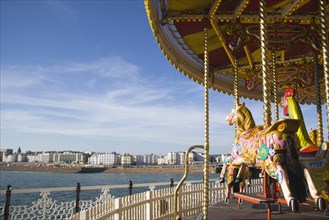 ENGLAND, East Sussex, Brighton, Empty fairground carrousel on Brighton Pier with the City and beach