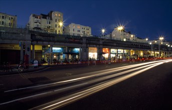 ENGLAND, East Sussex, Brighton, Seafront Promenade shops and bars illuminated at night with traffic