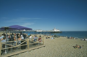 ENGLAND, East Sussex, Eastbourne, Beach Cafe with people sat on chairs under parasols and the pier