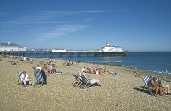 ENGLAND, East Sussex, Eastbourne, View across shingle beach with people sat on deckchairs towards