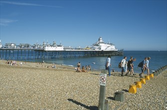 ENGLAND, East Sussex, Eastbourne, View across shingle beach towards pier with a group of people