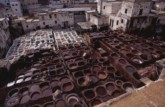 MOROCCO, Fes, Chouwara Tanneries.  Elevated view over the tanner’s pits with city buildings beyond.