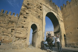 MOROCCO, Fes, Man leading mule carrying large load through horseshoe shaped arch of medina gateway.