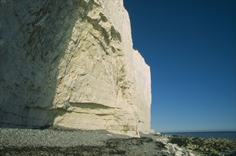 ENGLAND, East Sussex, Birling Gap, Base of cliff face partially in shadow with rockpools and pebble