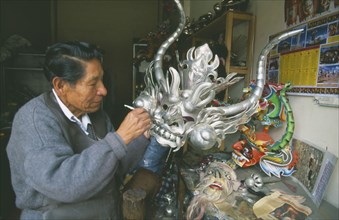 BOLIVIA, La Paz, Man painting a large silver mask.
