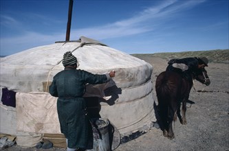 MONGOLIA, Gobi Desert , Herder mounting horse outside Yurt in the southern Gobi.