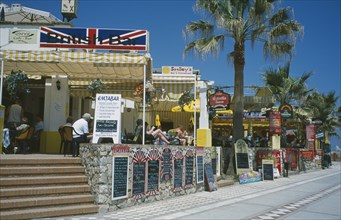 SPAIN, Andalucia, Benalmadena, Promenade with English restaurant and bar signs. People sat at