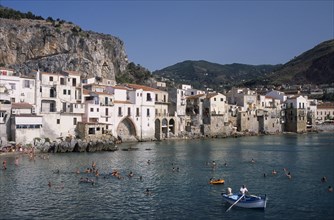 ITALY, Sicily, Palermo, Cefalu. View across people swimming in the sea next to sandy beach with a