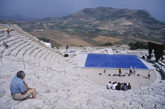 ITALY, Sicily, Segesta, Graeco Roman Amphitheatre. Man sat on steps looking down over stage area