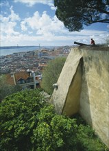 PORTUGAL, Lisbon, Visitor sitting on fortified walls beside cannon of Castelo de Sao Jorge  with
