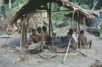 CONGO, Ituri Forest, Pygmies in village clearing sitting beneath thatched open sided shelter.