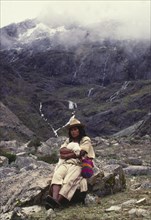 COLOMBIA, Santa Marta, Sierra Nevada , "Ica Indian with lamb sat on a rock, surrounded by mountains