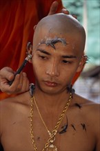 THAILAND, Bangkok, Novice monk having head shaved during ordination ceremony.