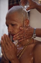 THAILAND, Bangkok, Novice monk having water poured over newly shaved head during ordination