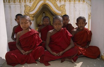 MYANMAR, Amarapura, Young novice monks meditating in front of shrine near Mandalay.