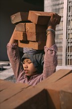 MYANMAR, Mandalay, Female construction worker carrying bricks on her head.