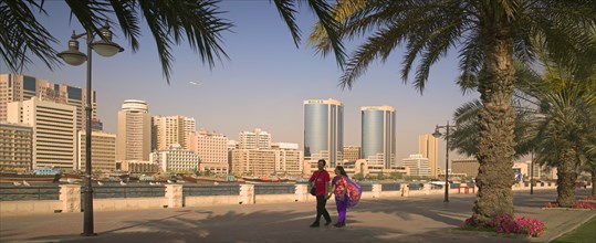 UAE, Dubai, View of Deira across Dubai Creek from Bur Dubai. A couple holding hands and palm trees